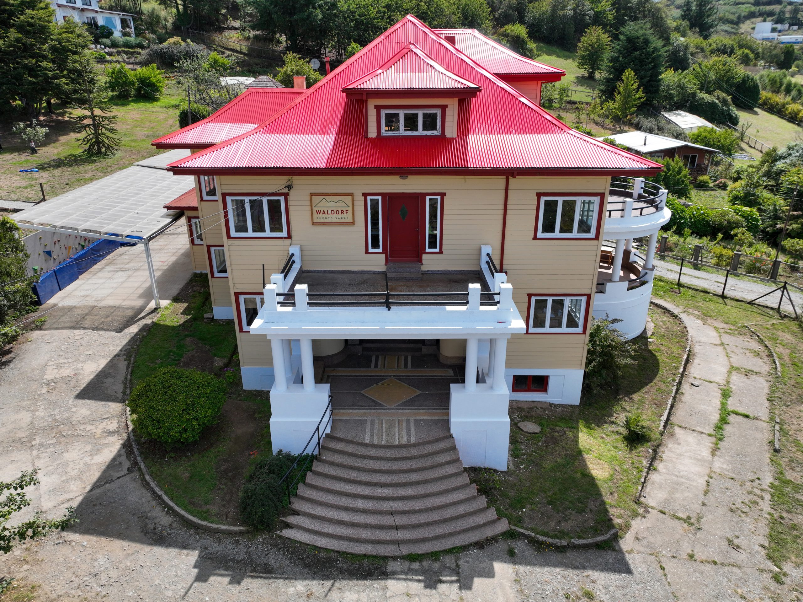 Casa grande de estilo arquitectónico con techo rojo, rodeada de vegetación y un camino de entrada.